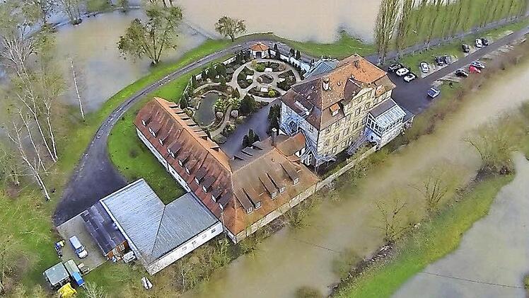 Mitunter mehrfach im Jahr wird das Denkmal an der Itz zum Wasserschloss, wie heuer im Februar (im Bild noch ohne Aufdach). Schlimm war es 2003, als "wir kurz vor einer Evakuierung standen, da das Wasser den Heizungsraum zu überschwemmen drohte und wir die Sandsäcke nur so schleppten", erinnert sich Peter Uhlig. Deutlich zu erkennen sind die Anbauten und der später an gelegte Park für alle Heimbewohner, wo Strandkörbe im Sommer einen Hinweis auf die Eigentümer geben. Sie stammen aus Bremen.  L...