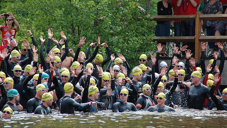 Vor dem Start im Trebgaster Badesee halten sich die Triathleten mit La-Ola-Übungen warm.