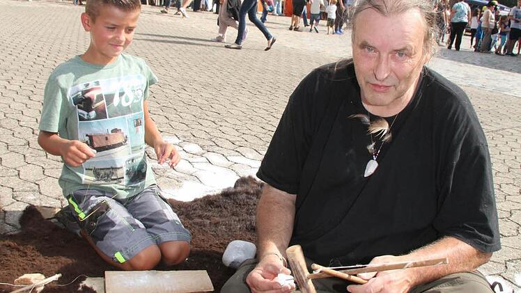 Walter Karl zeigt vor dem Indianertipi den Jungs, wie man mit einem Steinzeibohrer Löcher in Speckstein bekommt - und bei Dennis Hartmann (10) klappt es auch schon. Foto: Sonja Adam