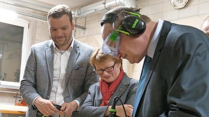 "Politik ist das lange Bohren dicker Bretter mit Leidenschaft und Phantasie", sagte einst Max Weber. In diesem Fall fräst Staatssekretär Michael Meister eine Kante an einem Brotzeitbrettchen ab, beobachtet von Creapolis-Leiter Markus Neufeld und Hochschulpräsidentin Christiane Fritze. Foto: Simone Bastian