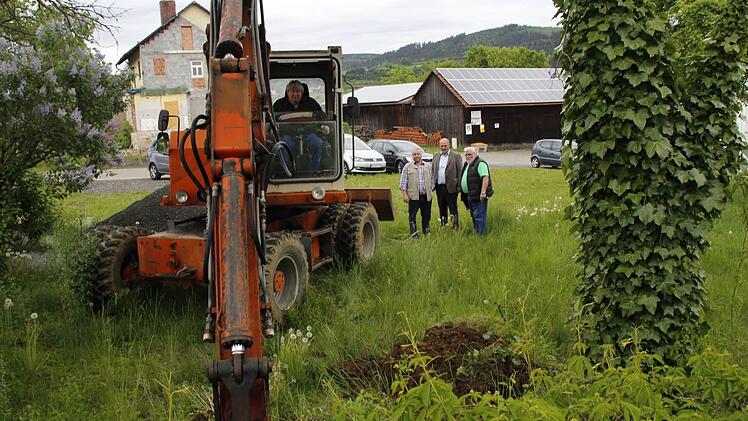 Bernd Wunder vom gleichnamigen Baggerbetrieb gräbt zur Bodenerkundung Erdreich auf dem Grundstück am Langenbühl ab, auf dem die Arztpraxis entstehen soll. Bürgermeister Ralf Holzmann (rechts, Mitte), sein Stellvertreter Fritz Rösch (links daneben) und Ingenieur Hans Spindler verfolgen gespannt, was die Baggerschaufel aus dem Untergrund zu Tage fördert. Foto: Matthias Beetz