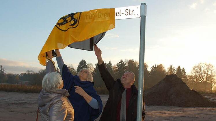 Hellmut Grempels Töchter Brigitte Maaser (links) und Clarissa Kob ziehen gemeinsam mit Oberbürgermeister Frank Rebhan die Fahne der Stadt Neustadt vom Schild für die Straße, die ab jetzt den Namen ihres Vaters trägt. Foto: Rainer Lutz