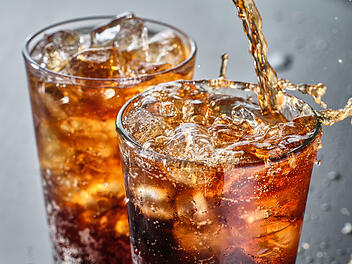 two cups of cola soft drink being poured into glass