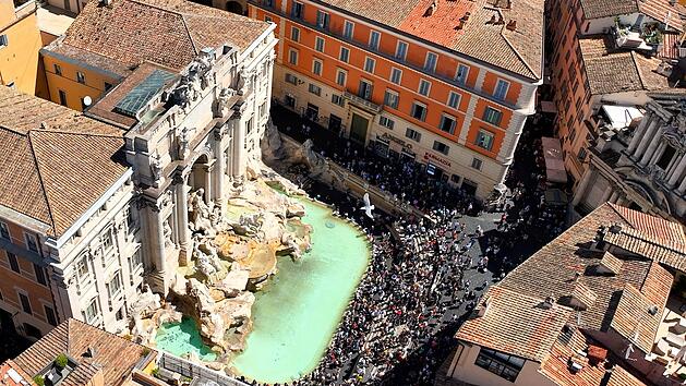 La fontana di Trevi a Roma, gremita di turisti, vista dall'alto. Ripresa aerea con drone della Fontana di Trevi piena di visitatori in una giornata estiva. Der Trevi-Brunnen in Rom, voller Touristen, von oben gesehen. Luftaufnahme mit einer Drohne vom Trevi-Brunnen, der an einem Sommertag voller Besucher ist.