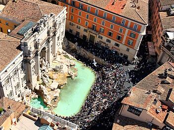 La fontana di Trevi a Roma, gremita di turisti, vista dall'alto. Ripresa aerea con drone della Fontana di Trevi piena di visitatori in una giornata estiva. Der Trevi-Brunnen in Rom, voller Touristen, von oben gesehen. Luftaufnahme mit einer Drohne vom Trevi-Brunnen, der an einem Sommertag voller Besucher ist.
