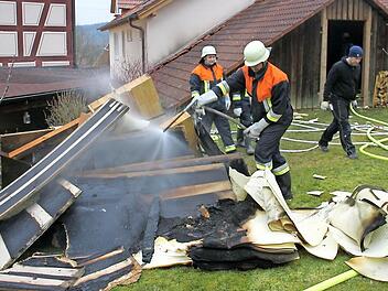 Feuerwehrleute löschen Holz- und Dämmmaterial, das sie vorher aus dem brennenden Dachstuhl (hinten) nach draußen schleppten.  Foto: A. Schmitt