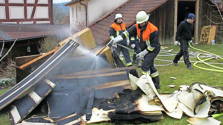 Feuerwehrleute löschen Holz- und Dämmmaterial, das sie vorher aus dem brennenden Dachstuhl (hinten) nach draußen schleppten.  Foto: A. Schmitt