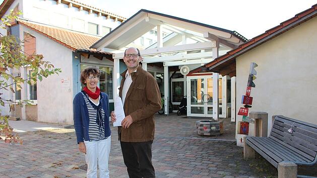 Claudia Straub und Dieter Muth vor dem Kindergarten St. Peter und Paul in Oberleichtersbach: Das Bestandsgeb&auml;ude wird in K&uuml;rze saniert. Der Neubau im hinteren Bereich ist fast fertig. Foto: Julia Raab