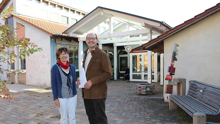 Claudia Straub und Dieter Muth vor dem Kindergarten St. Peter und Paul in Oberleichtersbach: Das Bestandsgebäude wird in Kürze saniert. Der Neubau im hinteren Bereich ist fast fertig. Foto: Julia Raab