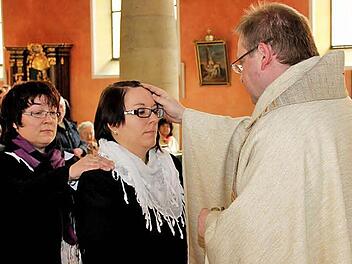 Patin Martina Dittner (links) legt Tina Menzel die Hand auf. Die 32-Jährige wird von Pfarrer Thomas Ringer gefirmt. Ihre Stirn wird mit Chrisam gesalbt. Fotos: Johanna Blum