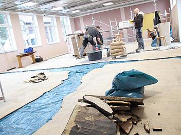 Zwei Bodenleger gießen die Lücken zwischen dem Asphaltestrich mit Epoxitestrich aus. Dort, wo vorher Wände im Hainer Kulturhaus standen oder der Asphalt weggebröckelt war, wurde blaue Folie auf den Beton gelegt, damit der neue Estrich nicht festklebt. Wenn diese Reparatur beendet ist, wird der Boden noch mit Gewebe gespachtelt. Dann kommt der Belag drauf. Die Hainer Bürger bringen am Samstag die Platten in der abgehängten Decke an.  Foto: Friedwald Schedel