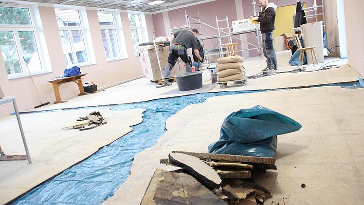 Zwei Bodenleger gießen die Lücken zwischen dem Asphaltestrich mit Epoxitestrich aus. Dort, wo vorher Wände im Hainer Kulturhaus standen oder der Asphalt weggebröckelt war, wurde blaue Folie auf den Beton gelegt, damit der neue Estrich nicht festklebt. Wenn diese Reparatur beendet ist, wird der Boden noch mit Gewebe gespachtelt. Dann kommt der Belag drauf. Die Hainer Bürger bringen am Samstag die Platten in der abgehängten Decke an.  Foto: Friedwald Schedel
