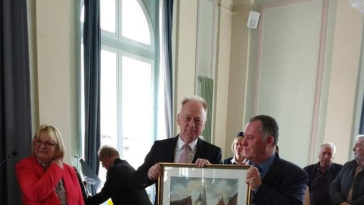 Bürgermeister Helmut Blank (links) überreicht ein Gemälde von der Altdtadt an Stéphane Perrin. Links im Bild Maria Knauff. Wilhelm Schmitt