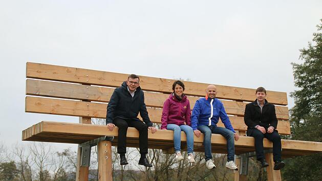 B&uuml;rgermeister Armin Warmuth, Annette Kolb und Christoph Sch&ouml;nau sowie Allianzmanager Holger Becker (von links) stellten die neue XXL-Holzbank offiziell vor. Sie steht am Radweg zwischen Obererthal und Thulba. Foto: Hilmar Ruppert