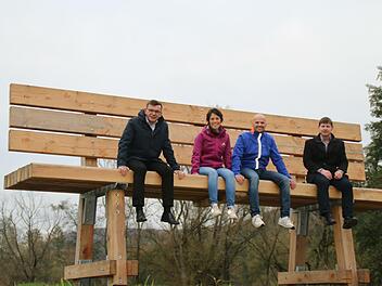 Bürgermeister Armin Warmuth, Annette Kolb und Christoph Schönau sowie Allianzmanager Holger Becker (von links) stellten die neue XXL-Holzbank offiziell vor. Sie steht am Radweg zwischen Obererthal und Thulba. Foto: Hilmar Ruppert