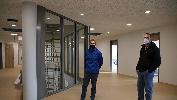 Im Obergeschoss: Die Öffnung hinunter zur Aula wurde verglast. Peter Karl (links) vom städtischen Baubüro und Schulleiter Michael Heyne haben ihre Schuhe ausgezogen, weil der Boden frisch eingelassen wurde. Foto: Ulrike Müller