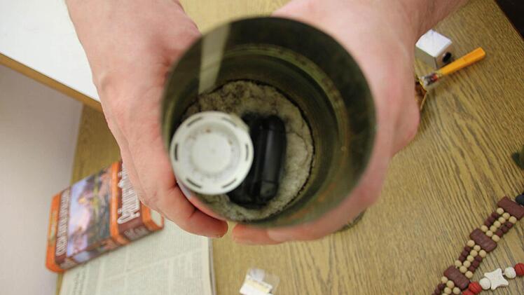 Handyversteck in einer Wurstdose. Die Plastikkapsel links in der Dose ist halb mit Wasser gefüllt und täuscht das Geräusch beim Schütteln einer Dose vor.