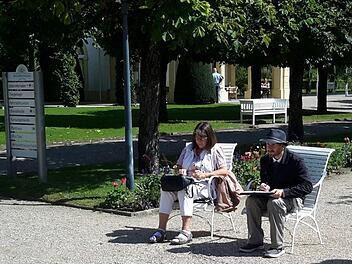 Auf der Mittelachse des Kurparks im Staatsbad haben die Urban Sketchers Claudia Körber und Milan Hoelzer Platz genommen: Ihr Blick geht diesmal zum Fürstenhof. Das Motiv des Tages zeichnet sie in ein kleines Notizbuch, er bringt es auf einem großen Block zu Papier.