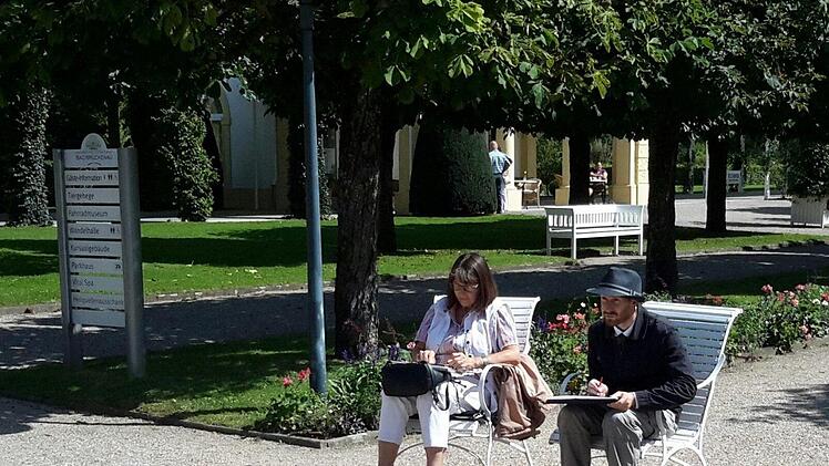 Auf der Mittelachse des Kurparks im Staatsbad haben die Urban Sketchers Claudia Körber und Milan Hoelzer Platz genommen: Ihr Blick geht diesmal zum Fürstenhof. Das Motiv des Tages zeichnet sie in ein kleines Notizbuch, er bringt es auf einem großen Block zu Papier.