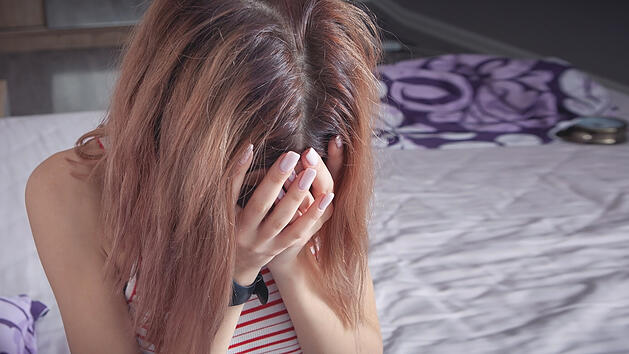 Frau sitzt mit Kopfschmerzen auf einem Bett.