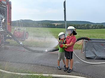 Linus (links) und Leon haben Spaß mit dem kindertauglichen Strahlrohr. Doch der Anlass ist ernst. Im Kampf gegen Flächenbrände auf Äckern oder Wäldern arbeiten Landwirte und Feuerwehren eng zusammen. Eine wichtige Rolle spielen dabei Faltbehälter (rechts im Bild). Foto: Rainer Lutz
