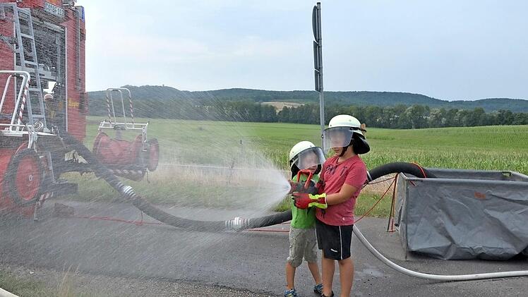Linus (links) und Leon haben Spaß mit dem kindertauglichen Strahlrohr. Doch der Anlass ist ernst. Im Kampf gegen Flächenbrände auf Äckern oder Wäldern arbeiten Landwirte und Feuerwehren eng zusammen. Eine wichtige Rolle spielen dabei Faltbehälter (rechts im Bild). Foto: Rainer Lutz