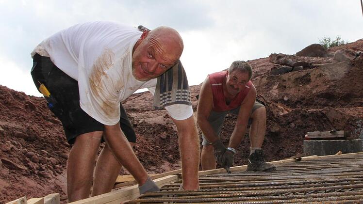 Bernd Neuf (links) und Bernhard Dittmayer verlegen Eisen für die Bodenplatte. Die Quelle wird nach oben hin abgedichtet, damit das Wasser nicht verschmutzt. Foto: Ulrike Müller