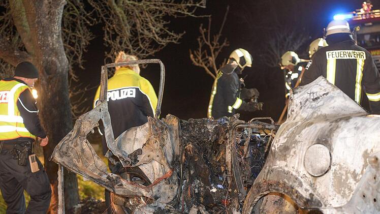 Sachsen-Anhalt, K&ouml;then: Feuerwehrleute und Rettungskr&auml;fte stehen auf einer Landstra&szlig;e hinter einem ausgebrannten Auto. Bei dem Autounfall sind drei Menschen, darunter ein Kind, verbrannt. Ein S&auml;ugling wurde aus dem Wrack gerettet. Foto: Heiko Rebsch/dpa-Zentralbild/dpa