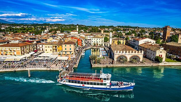 Altstadt und Hafen von Lazise: Lazise am Gardasee ist ein beliebter, malerischer Ort am s&uuml;d&ouml;stlichen Gardasee, der eine Mischung aus Geschichte, Kultur und Entspannung bietet. Die historische, autofreie Altstadt mit ihren alten Stadtmauern l&auml;dt zum Bummeln, Shopping und Genie&szlig;en in zahlreichen Caf&eacute;s und Restaurants ein. Der Ort ist ideal f&uuml;r Wassersport, Badeurlaube und Erholung an den Str&auml;nden oder in der Therme. Zudem ist Lazise ein guter Ausgangspunkt f&uuml;r Ausfl&uuml;ge und liegt in der N&auml;he von Freizeitparks wie Gardaland.