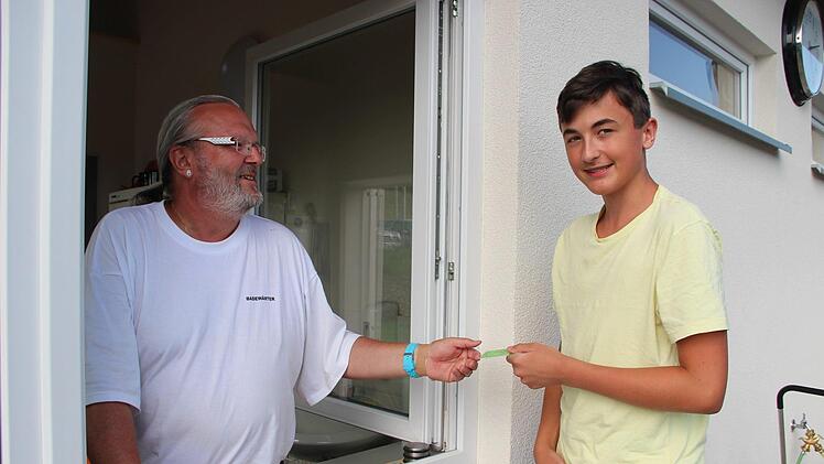 Michael Friedl zeigt Badewart Helmut Meyer an der Kasse des Freibades seine Dauerkarte.Heike Beudert