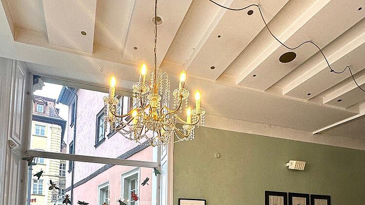 Ein gem&uuml;tliches Caf&eacute; mit Holzboden, Kastenfenster, einem Kronleuchter und Wandkunst. Rote und Holzm&ouml;bel bieten einladende Sitzm&ouml;glichkeiten.