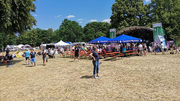 Ein Festival mit vielen Menschen, einer B&uuml;hne mit blauen Zelten, B&auml;nken und Essensst&auml;nden im Freien. Perfektes Wetter: blauer Himmel und Sonnenschein. Eine familienfreundliche Veranstaltung.