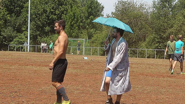 Beim Quattroball-Turnier in Memmelsdorf gingen die Hobbysportler auf dem Fußballplatz ganz unterschiedlich mit der Hitze um: Der eine entledigt sich seines Trikots, der andere schützt sich mit einem Sonnenschirm.sportpress