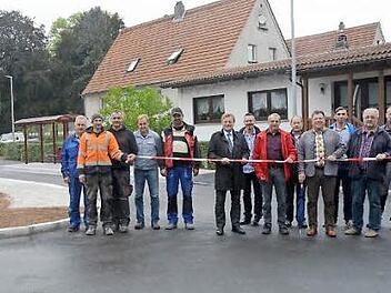 Unter den Augen von Vertretern der beteiligten Firmen und Gemeindevertretern durchschneidet Bürgermeister Rainer Detsch (6. v. l.) das Absperrband und gibt die Straße wieder für den Verkehr frei. Foto: K.- H. Hofmann