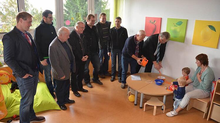 Jemie und Nico und ihre Erzieherin Ute Betz zeigen ihren Gästen wie schön es im Sonnenzimmer ist und welche schönen Spielsachen sie haben. Von links Thomas Pyka, Thorsten Michel, Günter Dobner, Pater Maximilian Kray, Sandro Selig, Jürgen Kolb, Julian Schmidt, Heinz Kraus, Bürgermeister Herbert Schneider. Foto: Karl-Heinz Hofmann