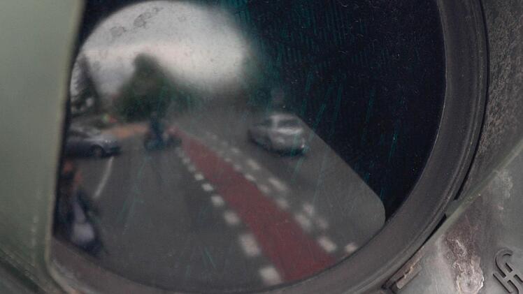 Der Verkehr spiegelt sich in einer dunklen Ampel-Scheibe.