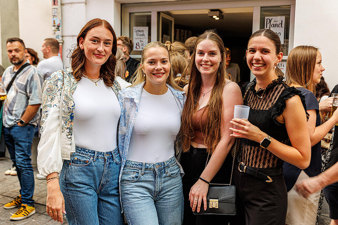 Gruppe von vier lachenden Frauen in Freizeitkleidung auf einer belebten Straße beim Bamberger Sandkerwa. Menschen im Hintergrund, einige mit Getränken. Stimmung fröhlich und entspannt.