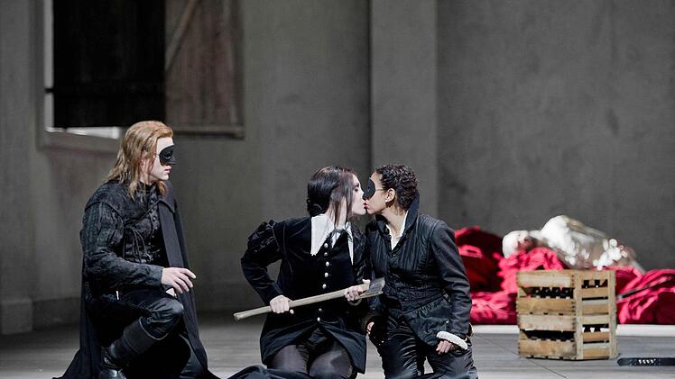 Don Ottavio (Martin Mitterrutzner) muss zuschauen, wie sich Donna Anna und Donna Elvira (Juanita Lasvarro) küssen. Alle drei gehen in Komtur- bzw. Don Giovanni-Kleidung zum Fest.