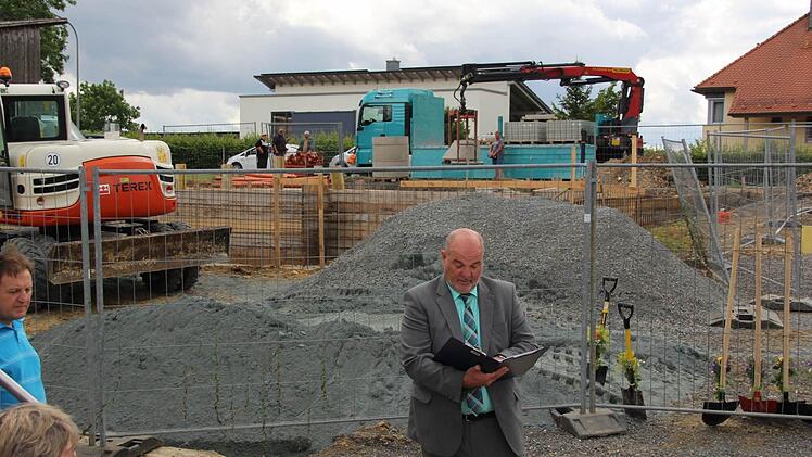 Typisch Rugendorf: Während Bürgermeister Ralf Holzmann auf den offiziellen Spatenstich einstimmt, wird schon Baumaterial geliefert. Foto: Matthias Beetz