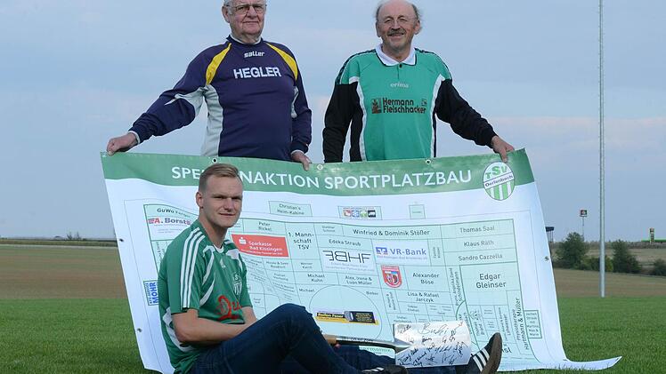 TSV-Vorsitzender Nico Rogge (sitzend), Paul Küthe (Mitglied Sportplatz-Kommission) und Architekt Burkard Kuhn (rechts) mit der Sponsoren-Tafel und dem Spaten als Symbol für den Sportplatz-Neubau. Foto: Jürgen Schmitt