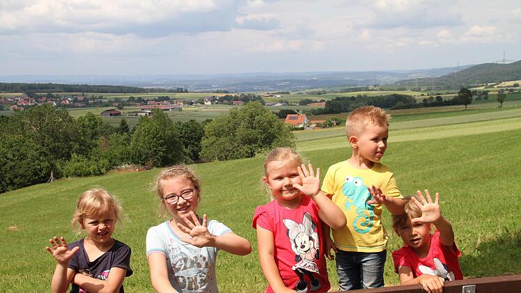 Vom Aussichtsplatz aus zeichnen sich fünf Windräder im Hintergrund ab, wie die Kinder mit ihren Fingern zeigen.