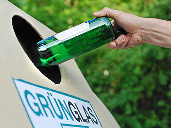 Mensch entsorgt eine Glasflasche in einem Altglas-Container f&uuml;r Gr&uuml;nglas