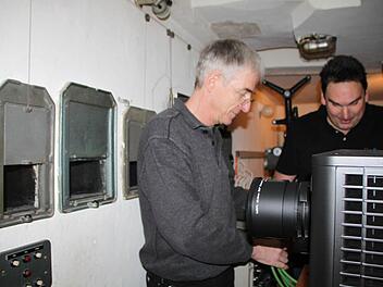 Rainer Mensing und Alexander Appel installieren den neuen Projektor. Die Linse wirft die Bilder durch eine der drei Öffnungen in der Wand. Foto: Ulrike Müller