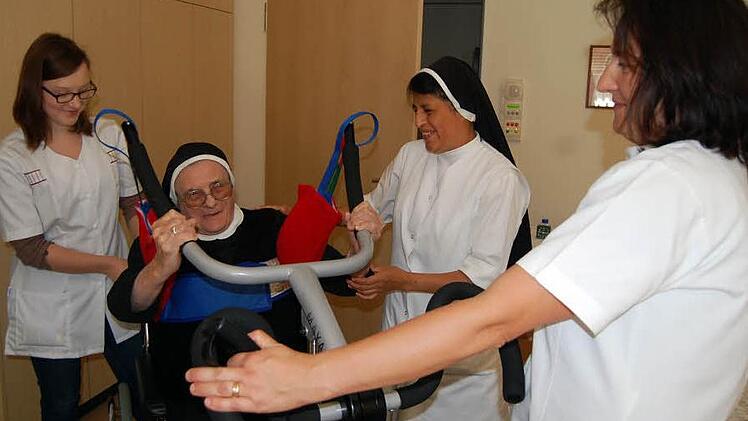Schwester Wendeline wird vom Sessel in den Rollstuhl gehoben. Es helfen (von links): Lena Passing, die ihr soziales Jahr in Vierzehnheiligen absolviert, Schwester Milagros und Pflegehelferin Silvia Hellmuth.