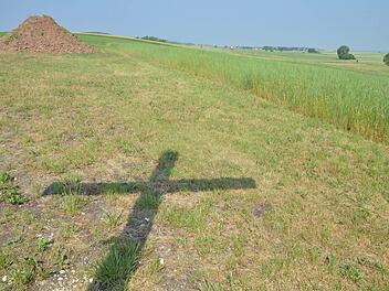 Der Schatten des Mahnkreuzes gegen den Flugplatzneubau fällt auf eine Wiese nahe dem Gelände, wo das Projekt umgesetzt werden soll. Foto: Rainer Lutz