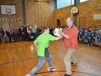 Mit einem lauten Ruf und einem schnellem Schlag durchschlägt Christian Kaim ein 1,8 Zentimeter starkes Brett in zwei Teile, das Ju-Jutsu Trainer Alfred Busse in Händen hält. Die Eltern, Großeltern, Mitschüler und auch Bürgermeister Rainer Detsch spenden Beifall.  Foto: Hofmann