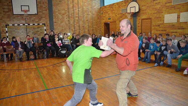 Mit einem lauten Ruf und einem schnellem Schlag durchschlägt Christian Kaim ein 1,8 Zentimeter starkes Brett in zwei Teile, das Ju-Jutsu Trainer Alfred Busse in Händen hält. Die Eltern, Großeltern, Mitschüler und auch Bürgermeister Rainer Detsch spenden Beifall.  Foto: Hofmann
