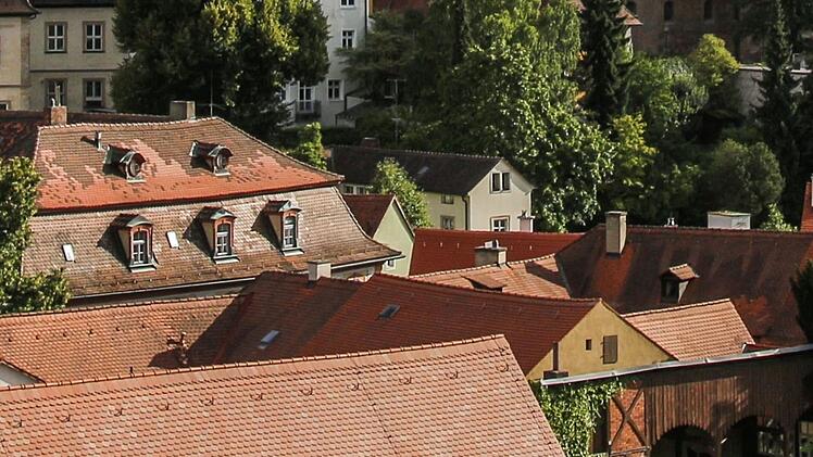 Eine idyllische Altstadt-Szene mit traditionellen H&auml;usern und roten Ziegeld&auml;chern, umgeben von gr&uuml;ner Vegetation. Ein fr&auml;nkisches Flair im Sonnenlicht.