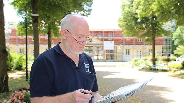 Christian Neugebauer betrachtet seine Sammlung alter Postkarten, die zeigen, wie sich die Brunnenlage im Inneren des Brunnenbaus (im Hintergrund) über die Jahre verändert hat. Foto: Charlotte Wittnebel-Schmitz