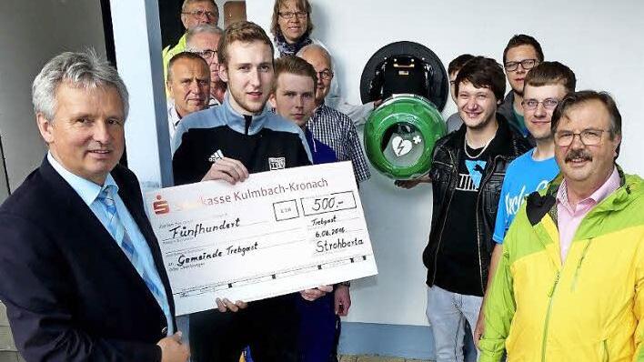 Bürgermeister Werner Diersch (vorne, links) freute sich bei der Vorstellung des neuen Defibrillators am Badesee über eine Spende, die Christian Kauper (mit Scheck) im Namen der "Strohberta" überreichte. Rechts der Vorsitzende der Trebgaster Wasserwacht und der Zweite Bürgermeister Albert Kolb Foto: Dieter Hübner